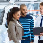 A salesman is shown speaking to a couple about their vehicle's trade in value.