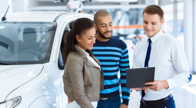 A salesman is shown speaking to a couple about their vehicle's trade in value.