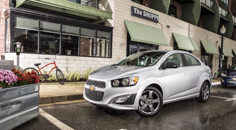 One of the most popular used cars near you, a silver 2016 Chevy Sonic RS, is shown parked on a city street.