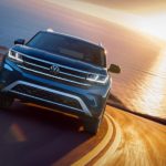 A popular used Volkswagen for sale, a dark blue 2018 Volkswagen Atlas SE, is shown driving away from the ocean.