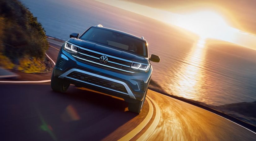 A popular used Volkswagen for sale, a dark blue 2018 Volkswagen Atlas SE, is shown driving away from the ocean.