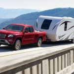 A red 2022 Nissan Frontier SV is shown from the front at an angle while towing a camper.