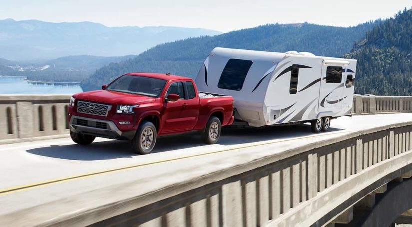 A red 2022 Nissan Frontier SV is shown from the front at an angle while towing a camper.
