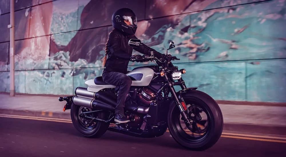 A white 2022 Harley-Davison Sportster S is shown from the side while driving past a wall.