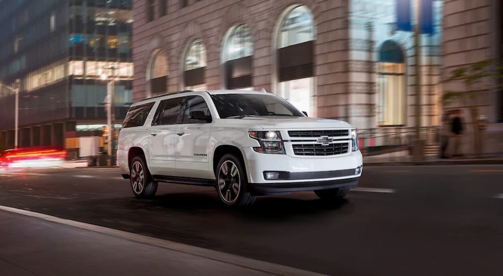 A popular used SUV for sale, a white 2020 Chevy Suburban is shown driving through a city at night.