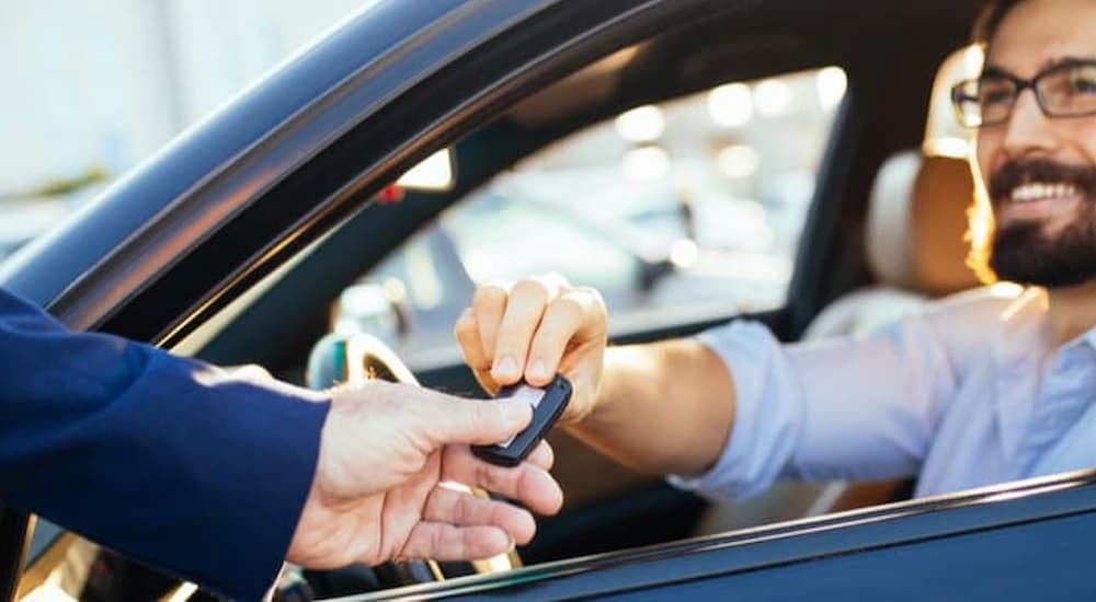 A person is shown handing a car key to a driver.