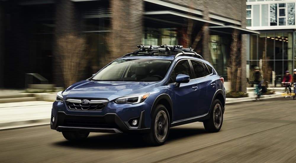 A blue 2023 Subaru Crosstrek is shown from the front at an angle while driving on a city street.