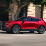 A red 2023 Chevy Blazer RS is shown driving on a city street after leaving a Chevrolet dealer.