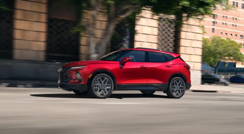 A red 2023 Chevy Blazer RS is shown driving on a city street after leaving a Chevrolet dealer.