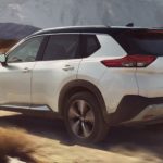 A white 2023 Nissan Rogue is shown from the side driving on a dirt road.