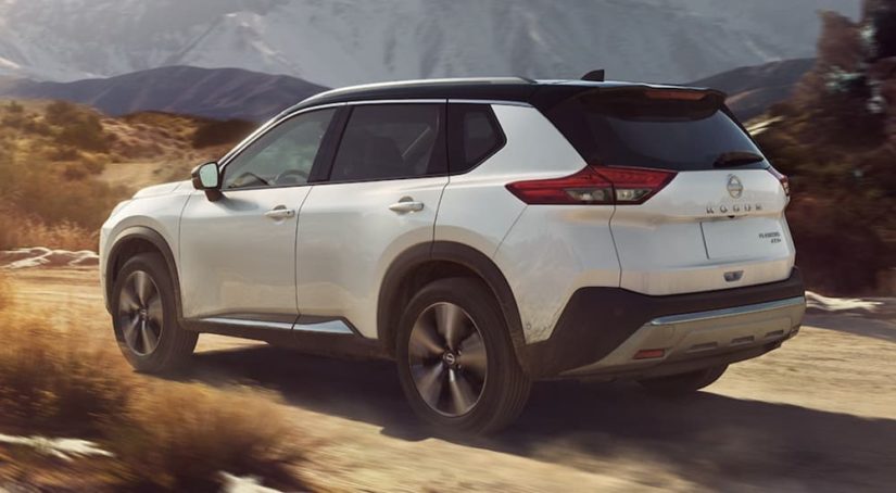 A white 2023 Nissan Rogue is shown from the side driving on a dirt road.