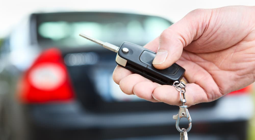 A person is shown unlocking a black sedan with a keyfob.