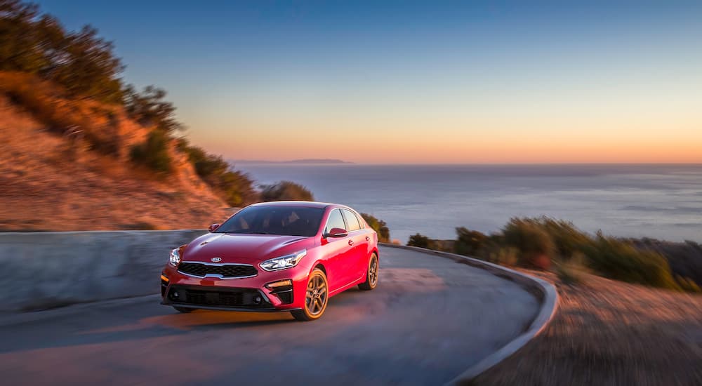 A red 2020 Kia Forte is shown from the front at an angle on a coastal road.