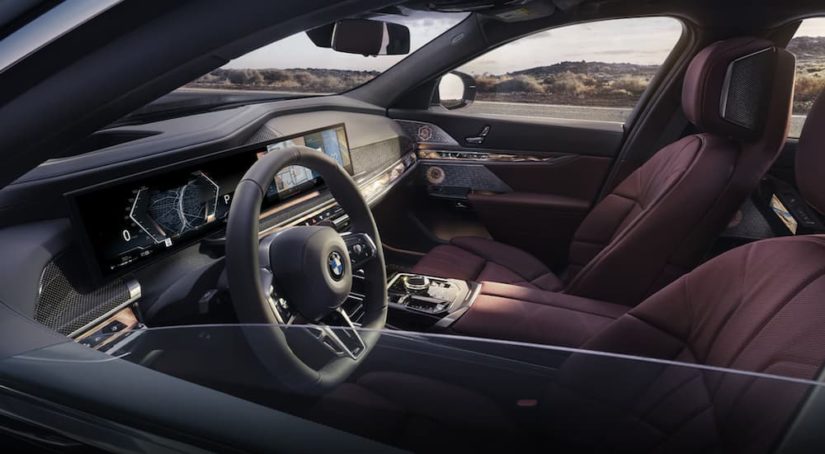 The red interior of a 2022 BMW 7-series shows the steering wheel and infotainment screen.
