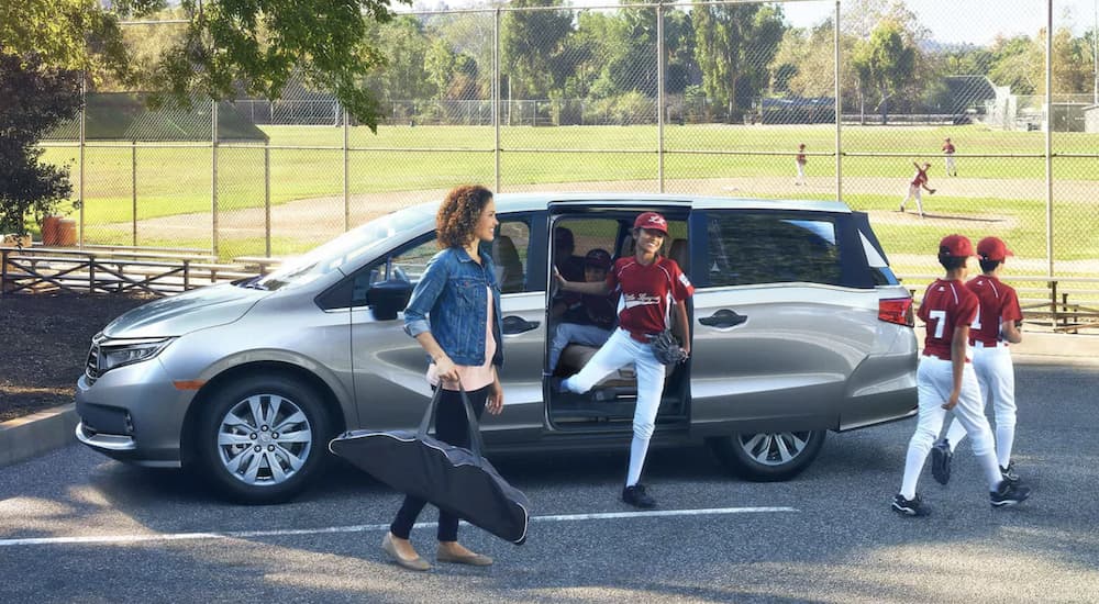 A silver 2023 Honda Odyssey Elite is shown parked at a baseball field as children get out of the vehicle.