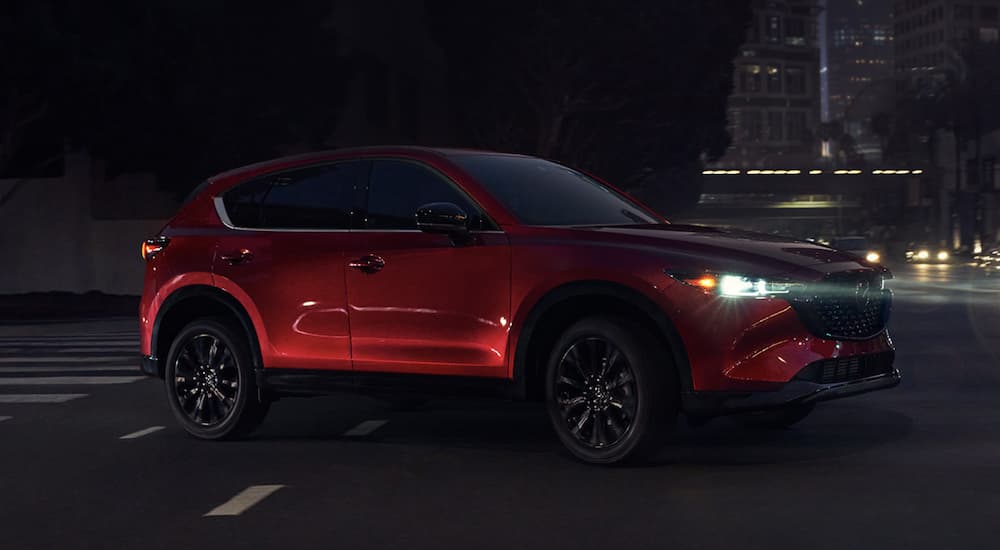 A red 2023 Mazda CX-5 is shown driving through a city.