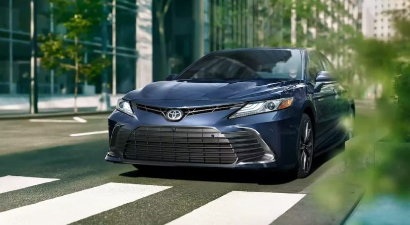 A blue 2023 Toyota Camry is shown on a city street.