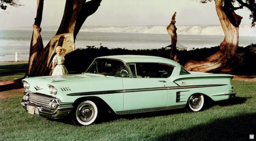 A lime green 1958 Chevy BelAir Impala is shown from the side parked in front of a ocean.