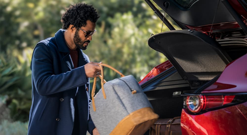 A person is shown stowing luggage in a red 2022 Mazda CX-30 after looking at a Mazda CX-30 for sale.