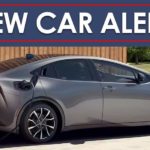 A silver 2023 Toyota Prius Prime XSE Premium is shown charging in a driveway below a new car alert banner.
