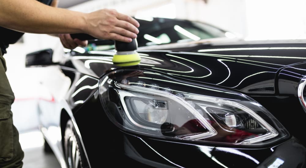 A person is shown polishing the hood of a black sedan.