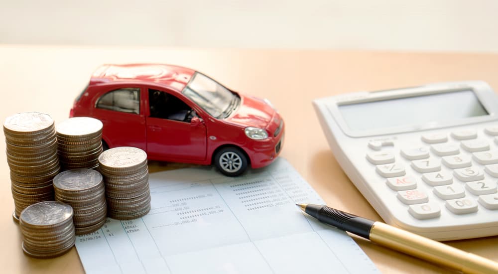 A red toy car is shown next to paperwork and coins.