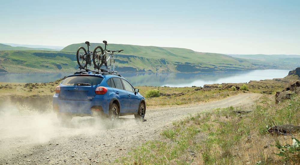 A blue 2017 Subaru Crosstrek is shown from a rear angle driving on a dusty dirt road.