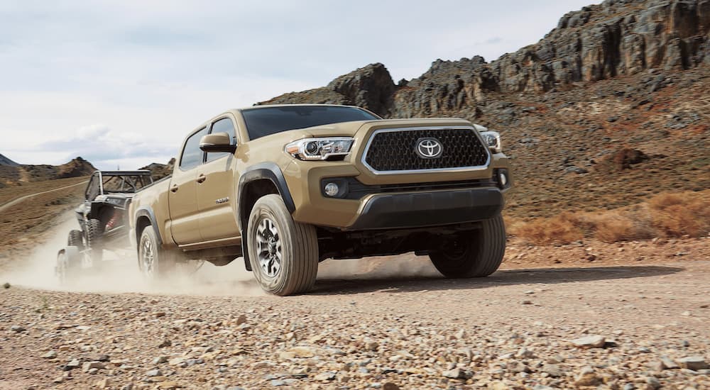 A tan 2019 Toyota Tacoma is shown driving on a dirt trail.