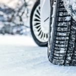 A snowy car is shown from a low angle after searching 'winter tires near me.'