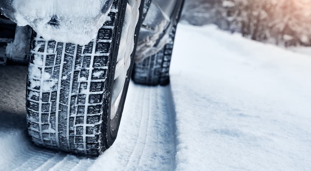 Tires on a car are shown making tracks in the snow.