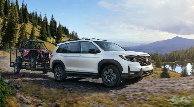 A white 2022 Honda Passport Elite is shown from the front while towing a UTV on a dirt trail after leaving a dealer that had SUVs for sale.