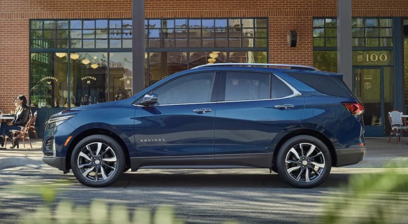 A blue 2023 Chevy Equinox is shown from the side parked in front of a brick building.
