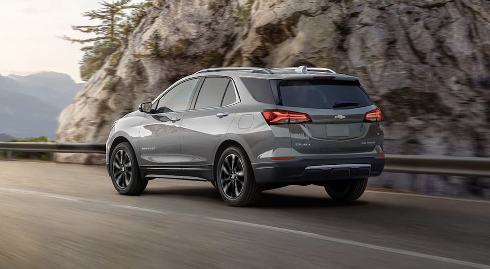 A grey 2023 Chevy Equinox is shown from the rear driving on an open road.