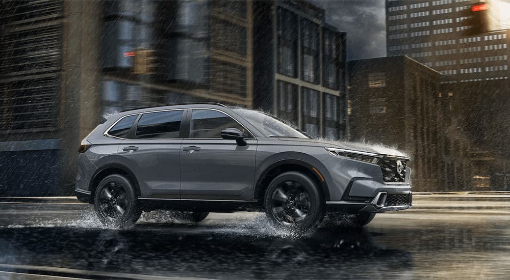 A grey 2023 Honda CR-V is shown from the side driving on a city street during a rain storm.