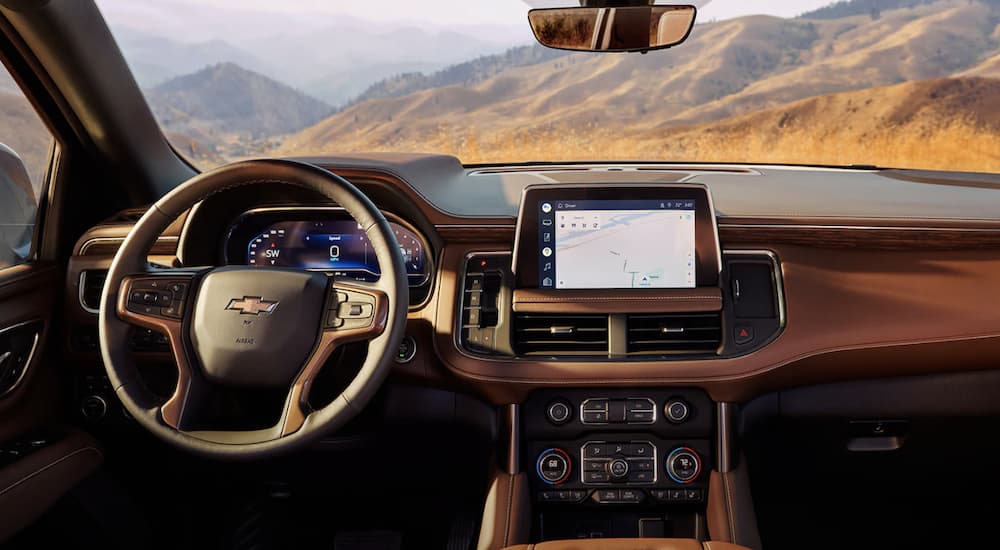 The brown interior of a 2023 Chevy Suburban shows the steering wheel and infotainment screen.
