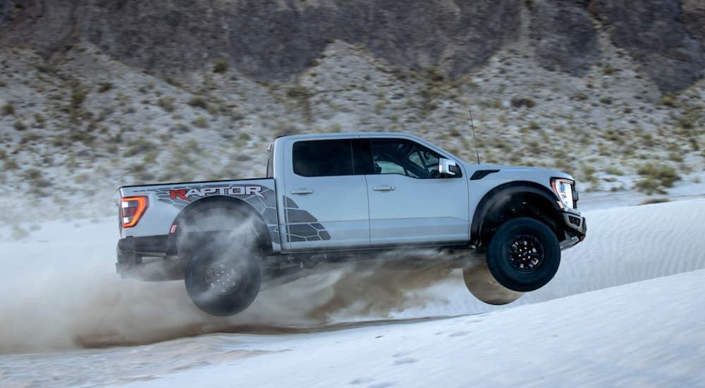 A silver 2023 Ford F-150 Raptor R is shown from the side while jumping over sand.