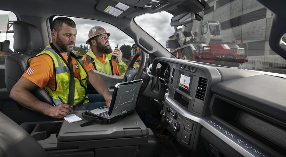 A construction worker is shown sitting in the driver's seat of a 2023 Ford F-250 while another worker stands by the door.