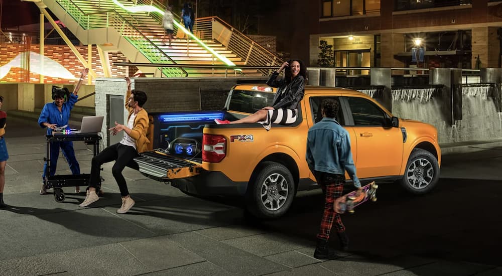 An orange 2023 Ford Maverick is shown from the side during a tailgate party.