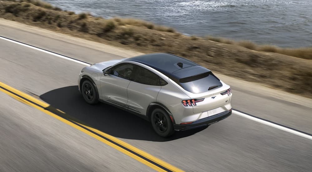 A white 2023 Ford Mustang Mach-E is shown driving on an open road.