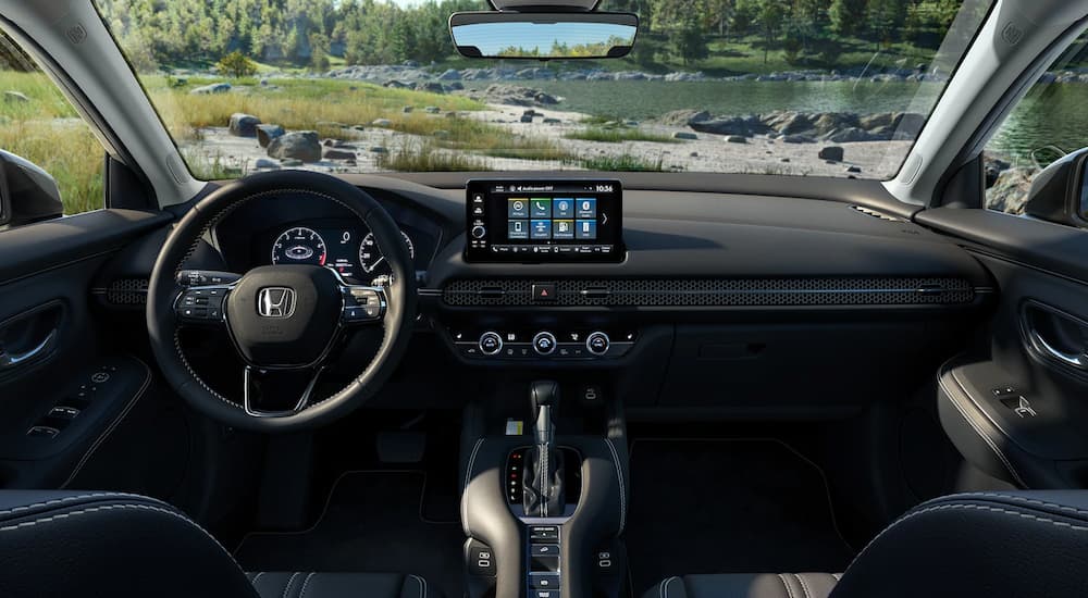 The black interior of a 2023 Honda HR-V shows the dashboard and steering wheel with a lake view.