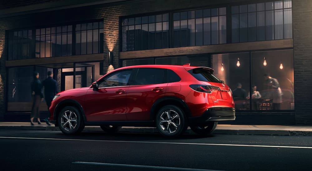 A red 2023 Honda HR-V EX-L is shown from the side while parked on the side of a city street.