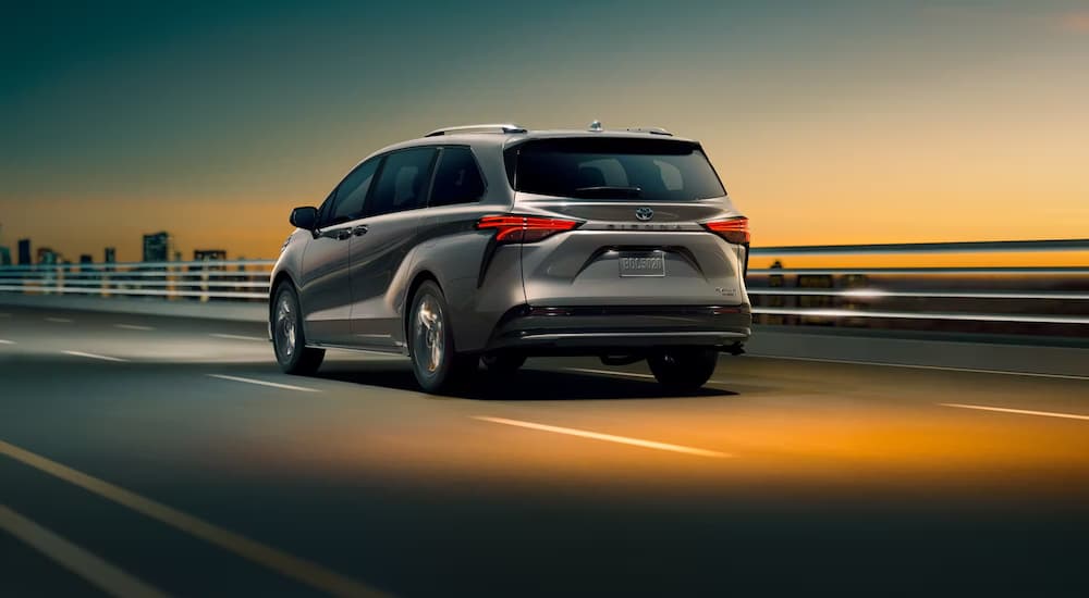 A grey 2023 Toyota Sienna Platinum Hybrid is shown driving over a city bridge at night.