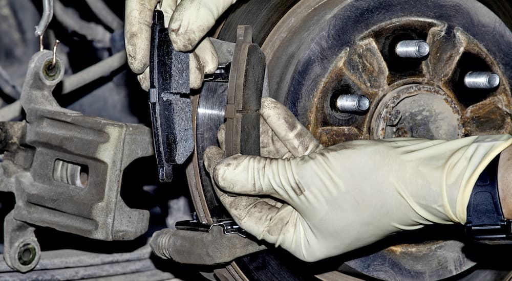 Gloved hands are shown holding a new and an old brake pad.