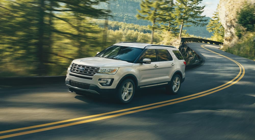 A white 2017 Ford Explorer is shown rounding a corner on a tree-lined road.