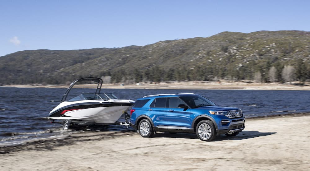 A blue 2020 Ford Explorer Hybrid is shown towing a boat next to a lake.