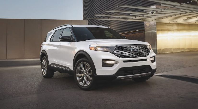 A white 2021 Ford Explorer Platinum Hybrid is shown in front of a modern building after leaving a Certified Pre-Owned Ford Explorer dealer.