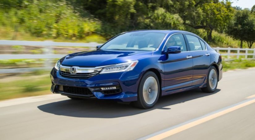 A blue 2017 Honda Accord is shown driving on a road next to a fence.