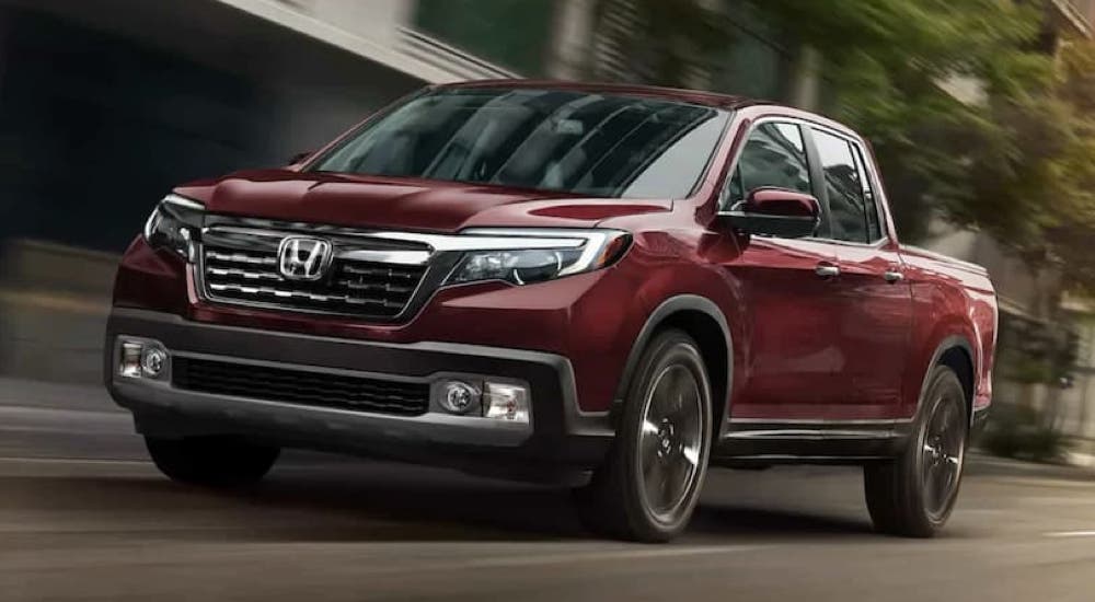 A red 2020 Honda Ridgeline RTL-E is shown driving on a highway near city buildings.