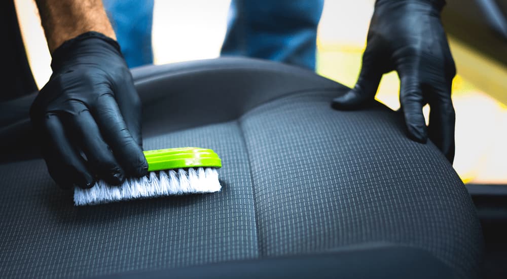 A person is shown using a brush to inspect the interior of a used vehicle.