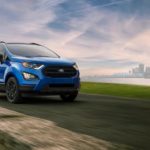 A blue 2022 Ford EcoSport is shown driving past a city and water.